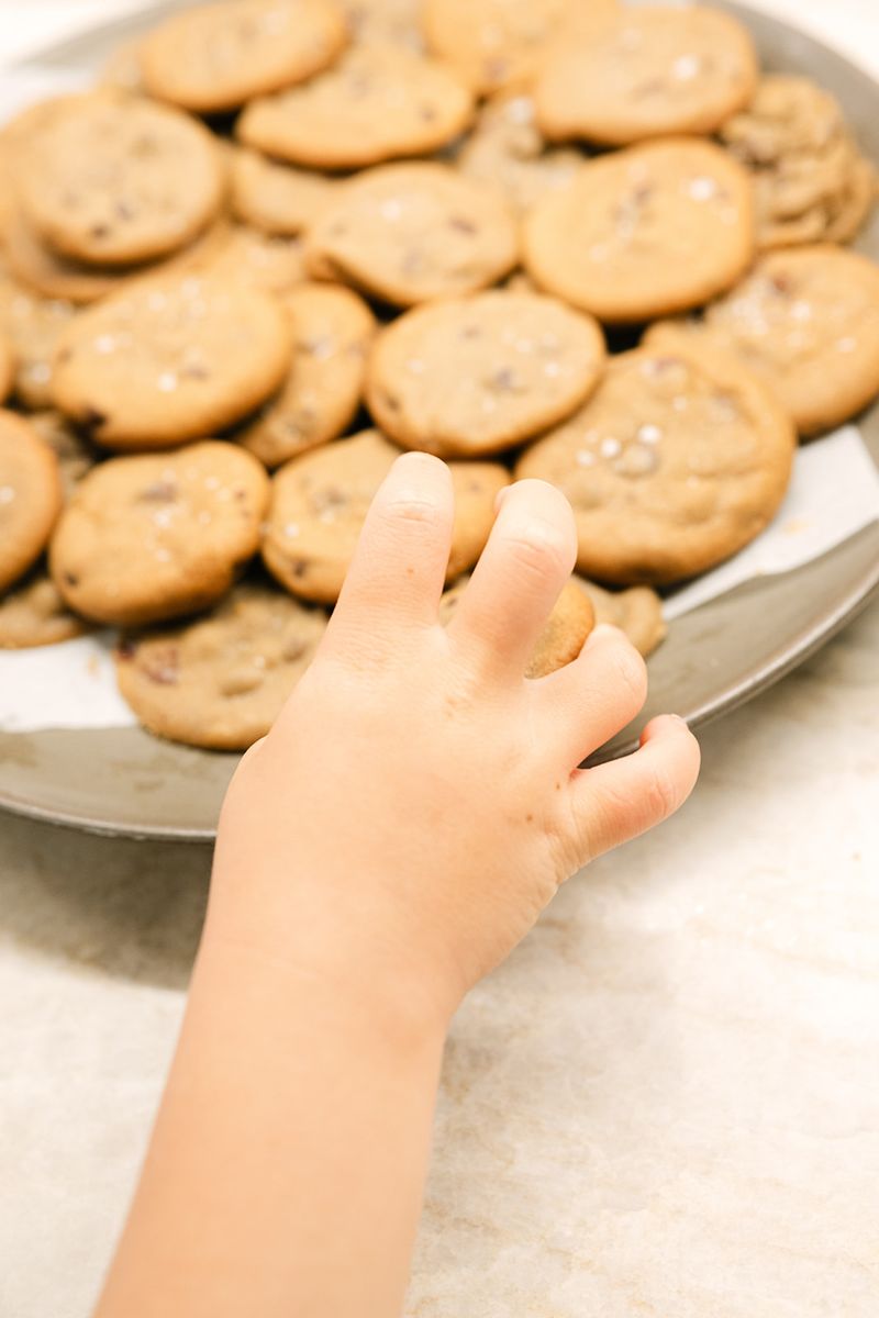 A small hand reaching for a chocolate chip cookie