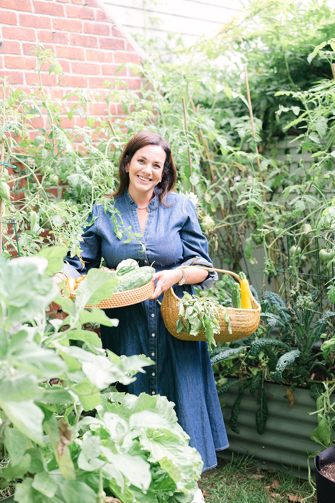 Brittney in her vegetable garden holding a tray and a basket of just-picked vegetables